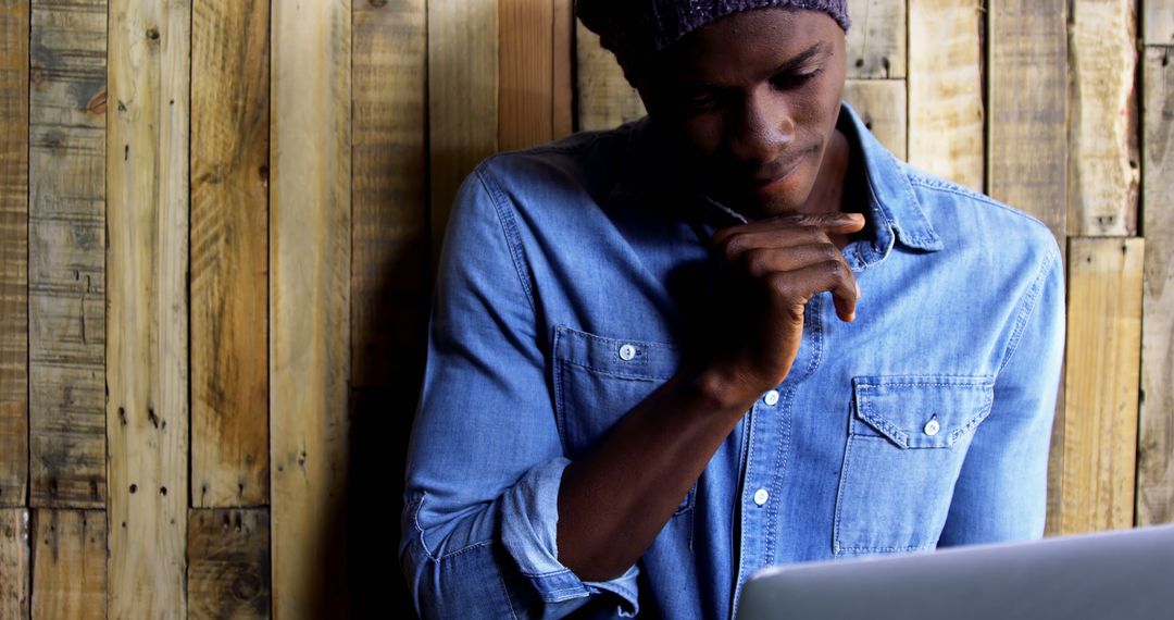 Pensive Man Using Laptop in Rustic Cafe Wearing Denim Shirt