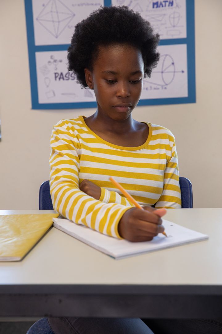 Focused Student Writing in Classroom with Yellow Striped Shirt