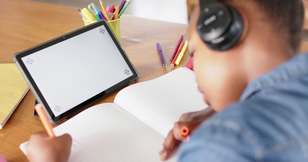 Young Student Writing in Notebook with Tablet on Desk - Free Images, Stock Photos and Pictures on Pikwizard.com