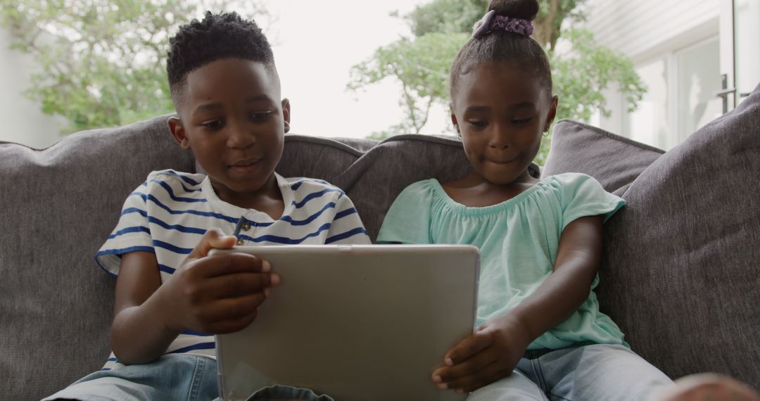 Two Happy Children Sharing Digital Tablet on Couch - Free Images, Stock Photos and Pictures on Pikwizard.com