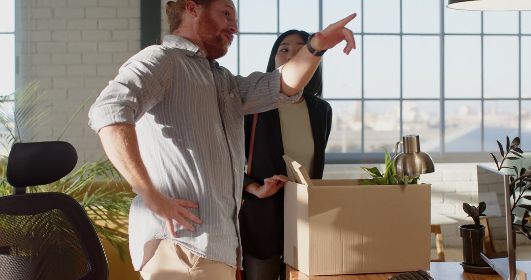 Colleagues Discuss Office Relocation with Cardboard Box and Desk Plant