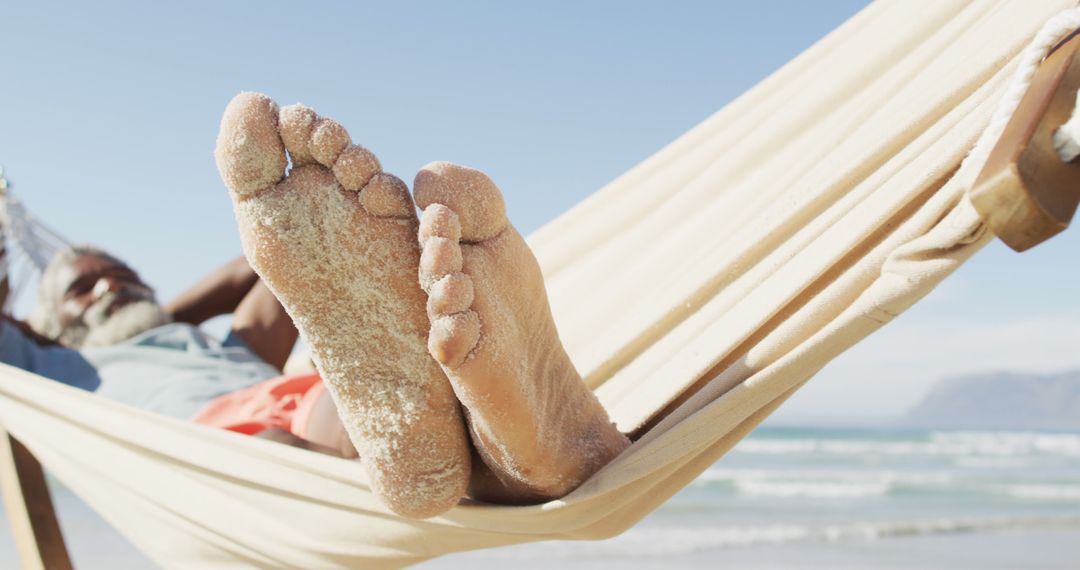 Relaxed man lying in hammock with sandy feet on beach enjoying vacation - Free Images, Stock Photos and Pictures on Pikwizard.com