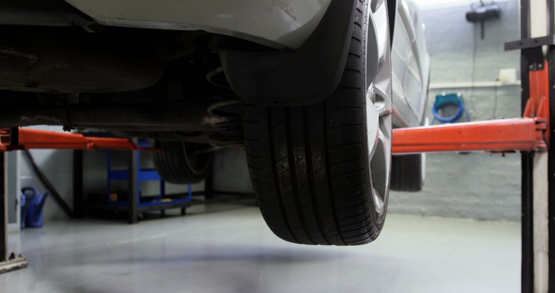 Car lifted in auto repair shop with visible tire and equipment - Free Images, Stock Photos and Pictures on Pikwizard.com