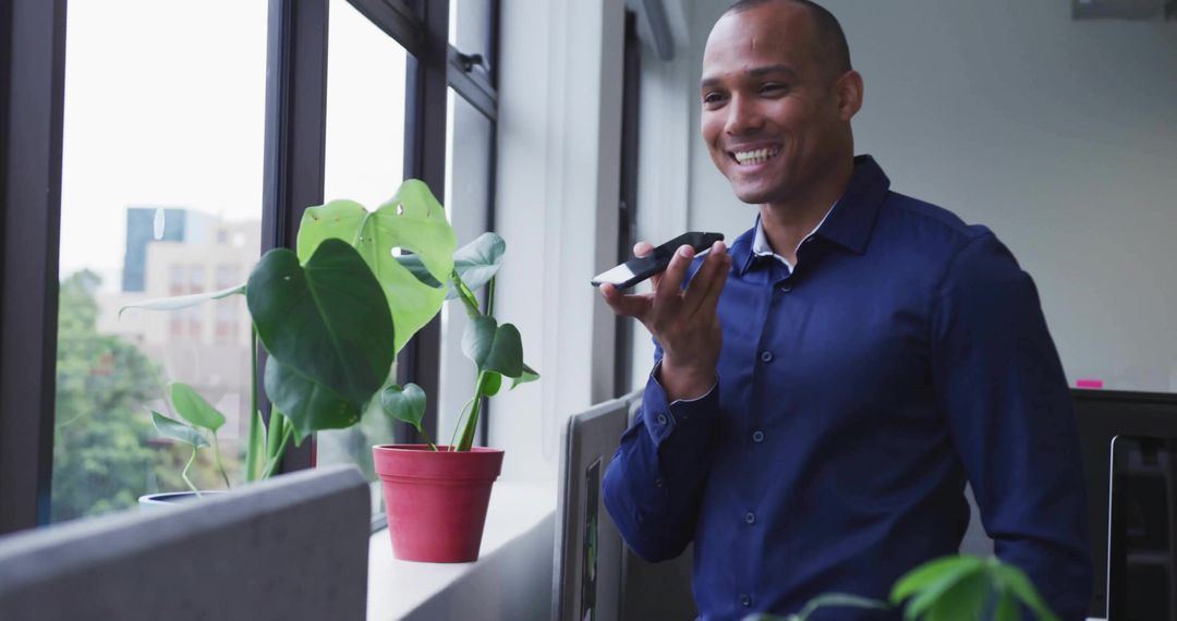 Smiling Professional Speaking Into Smartphone by Office Window