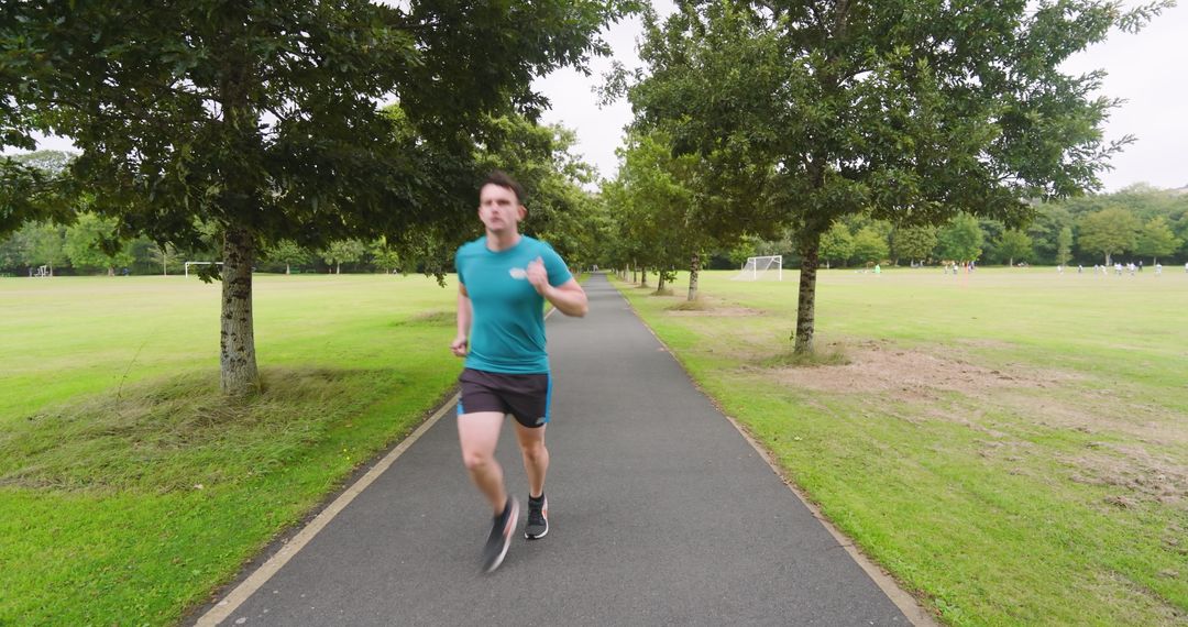 Man Jogging on Park Pathway Surrounded by Lush Greenery