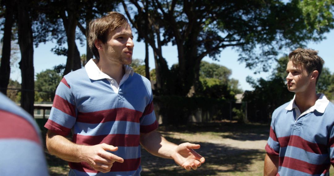 Teammates Gesturing and Listening in Sunlit Pine Clearing Wearing Matching Rugby Jerseys