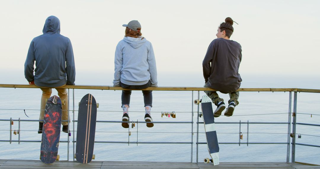 Three Friends Sitting on Fence With Skateboards by Ocean - Free Images, Stock Photos and Pictures on Pikwizard.com