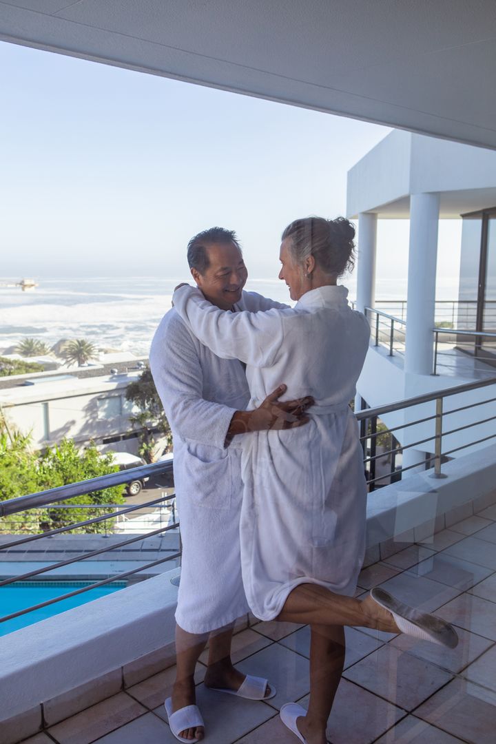 Senior Couple Embracing on Balcony Overlooking Ocean in Luxury Setting