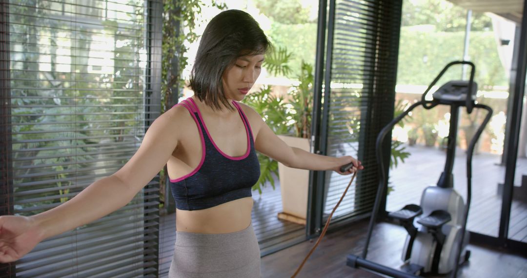 Focused asian woman holding skipping rope in sunny home gym - Free Images, Stock Photos and Pictures on Pikwizard.com