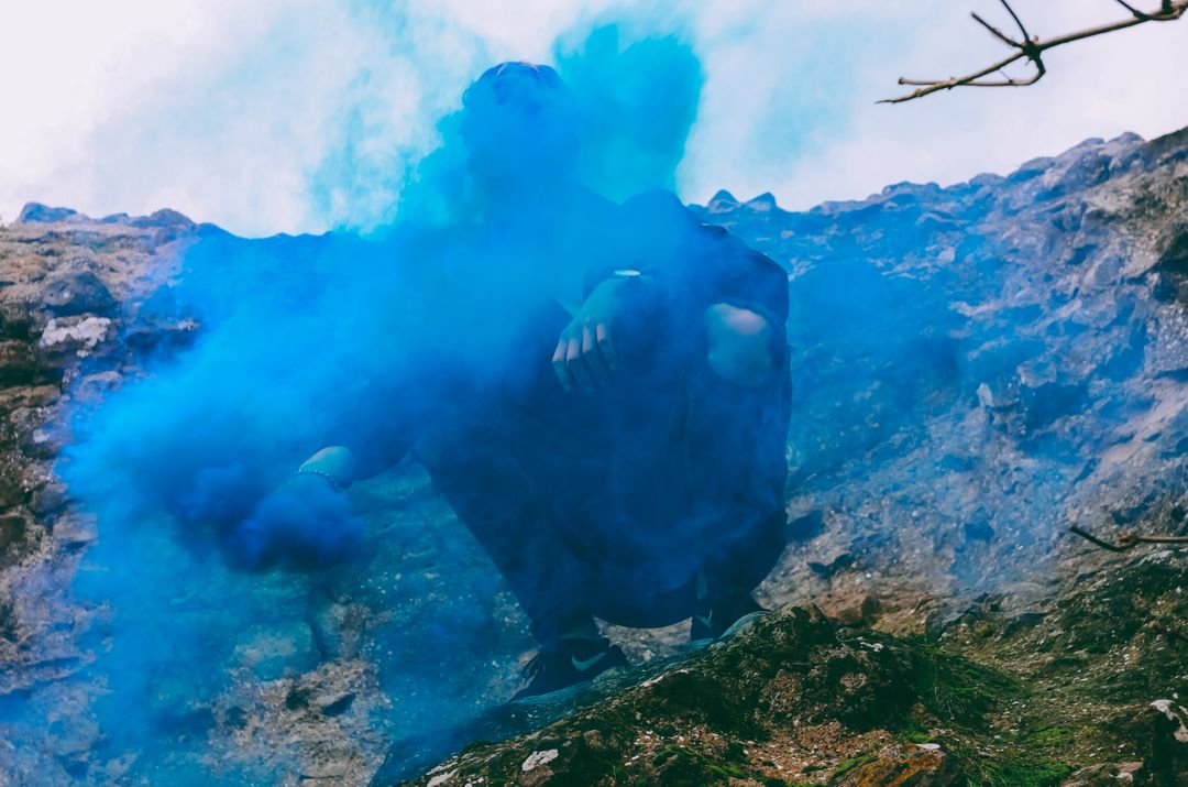 Person Covered in Blue Smoke amidst Rocky Terrain - Free Images, Stock Photos and Pictures on Pikwizard.com