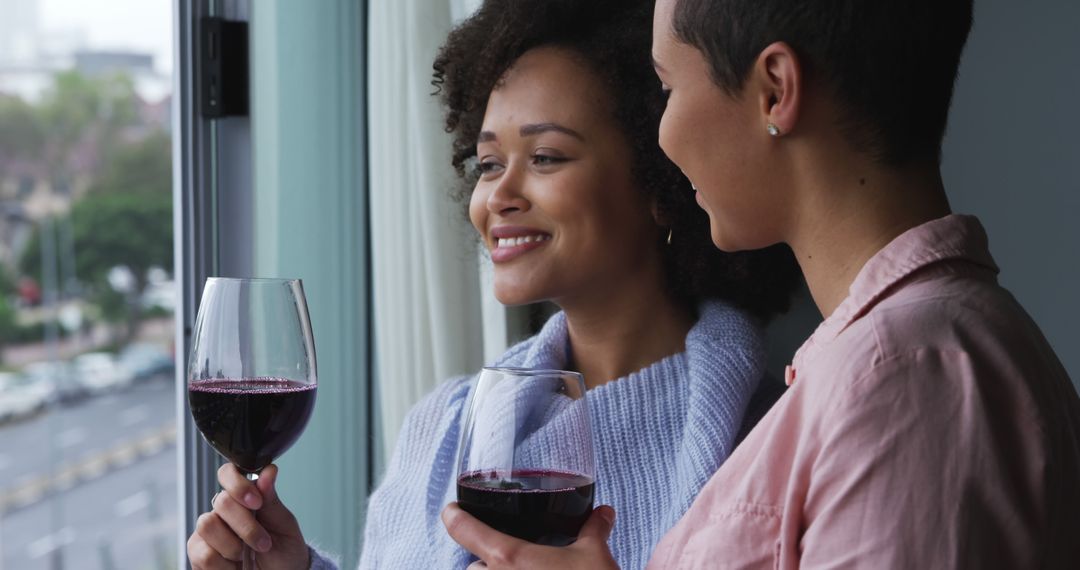 Two Women Enjoying Red Wine by Window, Smiling and Relaxing Together - Free Images, Stock Photos and Pictures on Pikwizard.com