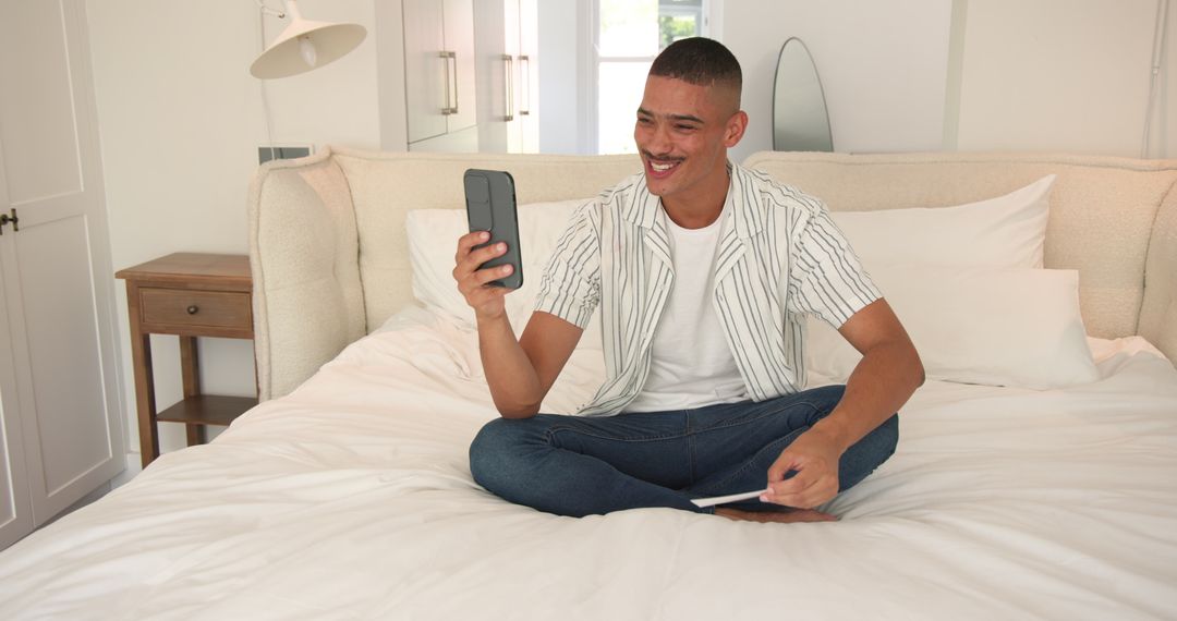 Young Man Sitting on Bed Using Smartphone Indoor Relaxation