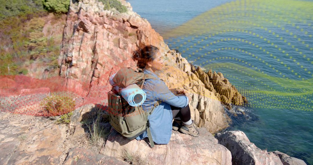 Hiker Sits Peacefully atop Rocky Cliff Overlooking Ocean Scenery