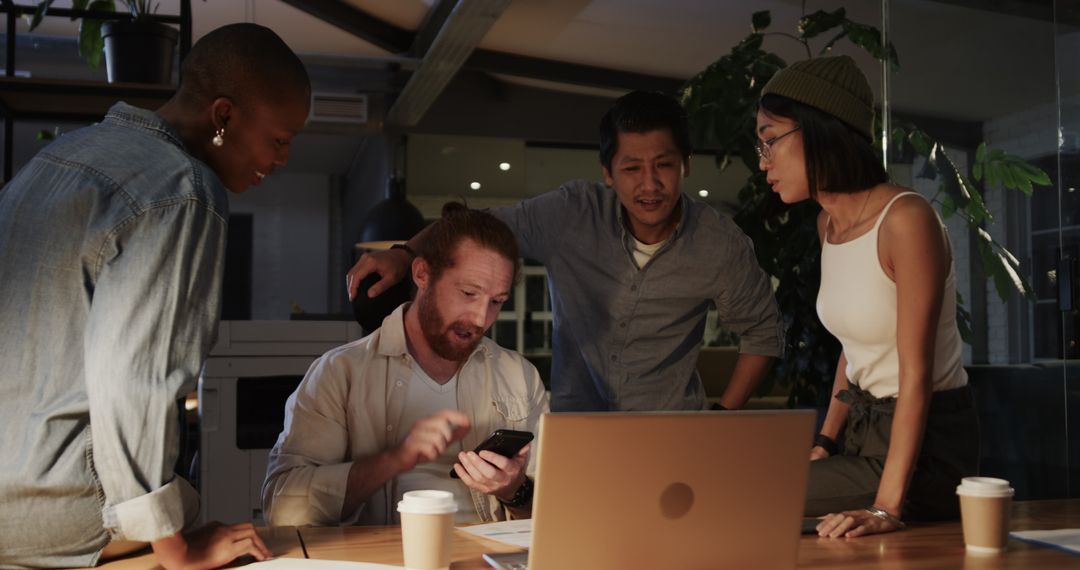Diverse Team Collaborating Enthusiastically Around Laptop at Night