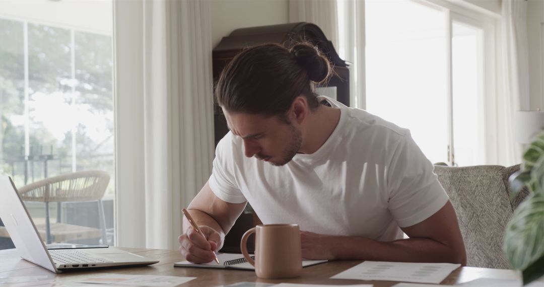 Man Focused on Remote Work at Home with Laptop and Notepad
