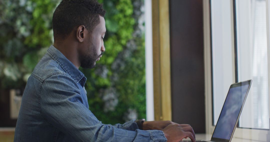 Focused African American Man Working on Laptop Overlooking Indoor Garden - Free Images, Stock Photos and Pictures on Pikwizard.com