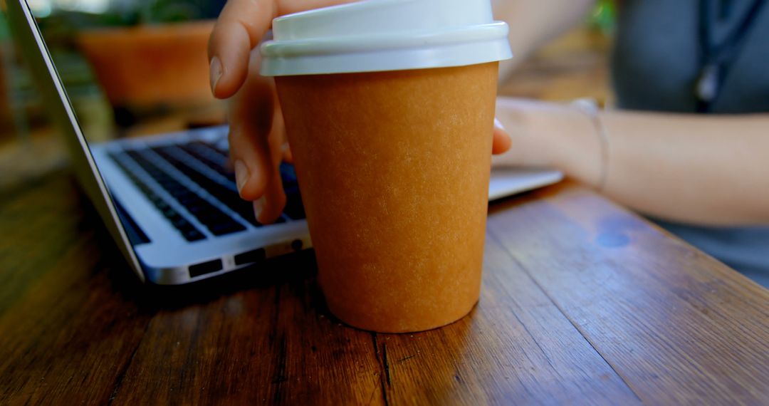 Person Working on Laptop with Coffee To-Go on Wooden Table - Free Images, Stock Photos and Pictures on Pikwizard.com