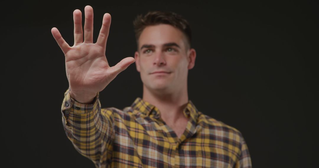 Young Man Holding Hand Up in Calm Gesture Against Dark Background - Free Images, Stock Photos and Pictures on Pikwizard.com