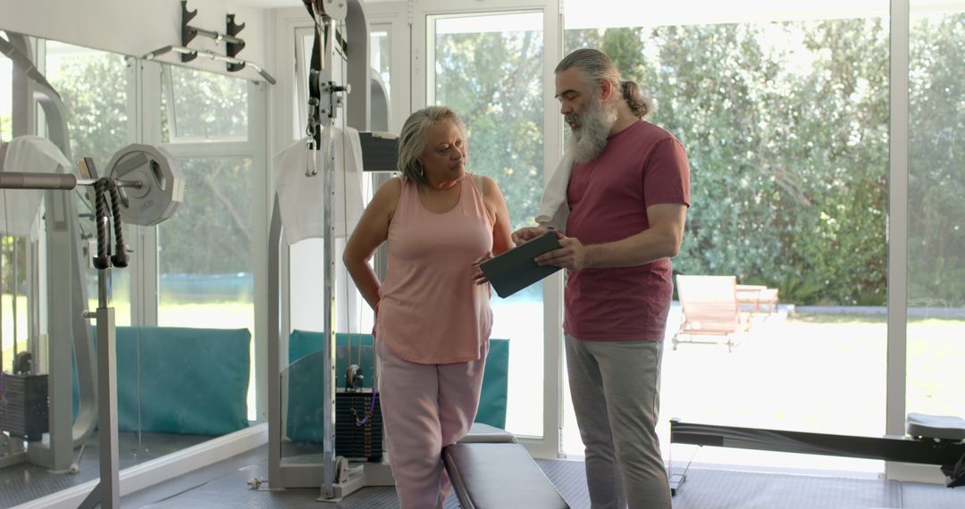 Senior Couple Discussing Fitness Plan in Home Gym with Tablet