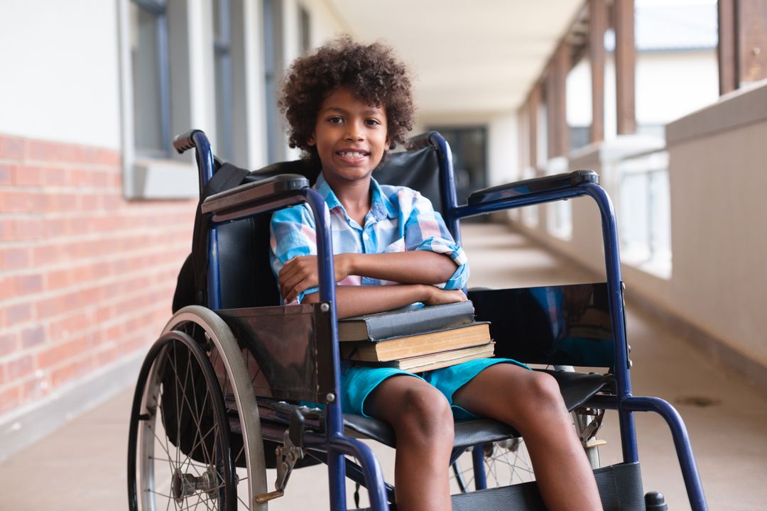 Portrait of african american elementary schoolboy with books sitting on wheelchair in corridor - Free Images, Stock Photos and Pictures on Pikwizard.com