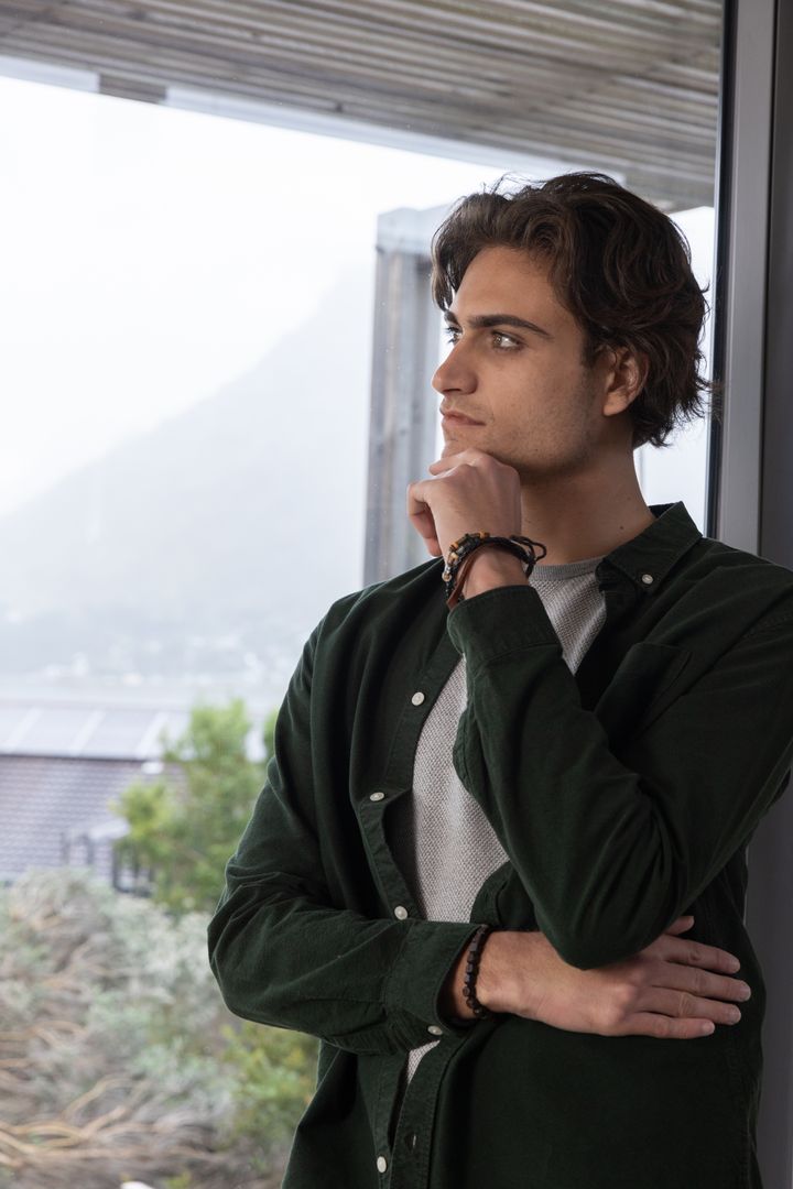 Contemplative Man Stands by Window Overlooking Misty Mountain