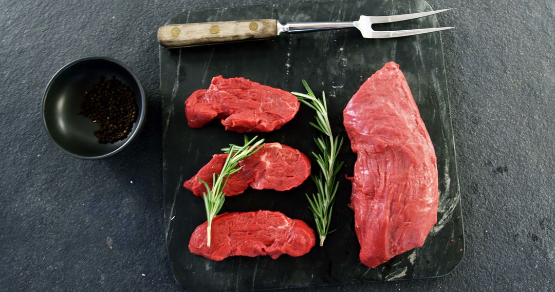 Raw Beef Steaks and Herb with Meat Fork on Black Surface - Free Images, Stock Photos and Pictures on Pikwizard.com