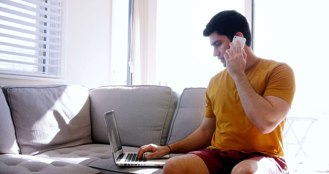 Young Man Working From Home on Laptop While Talking on Phone - Free Images, Stock Photos and Pictures on Pikwizard.com