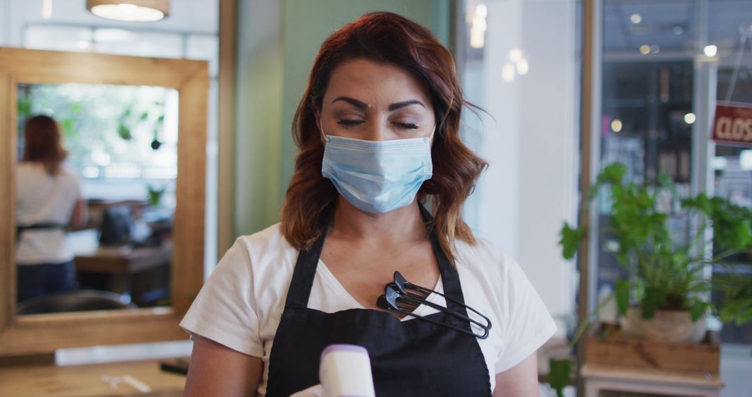 Female hairstylist in salon wearing face mask and apron - Free Images, Stock Photos and Pictures on Pikwizard.com