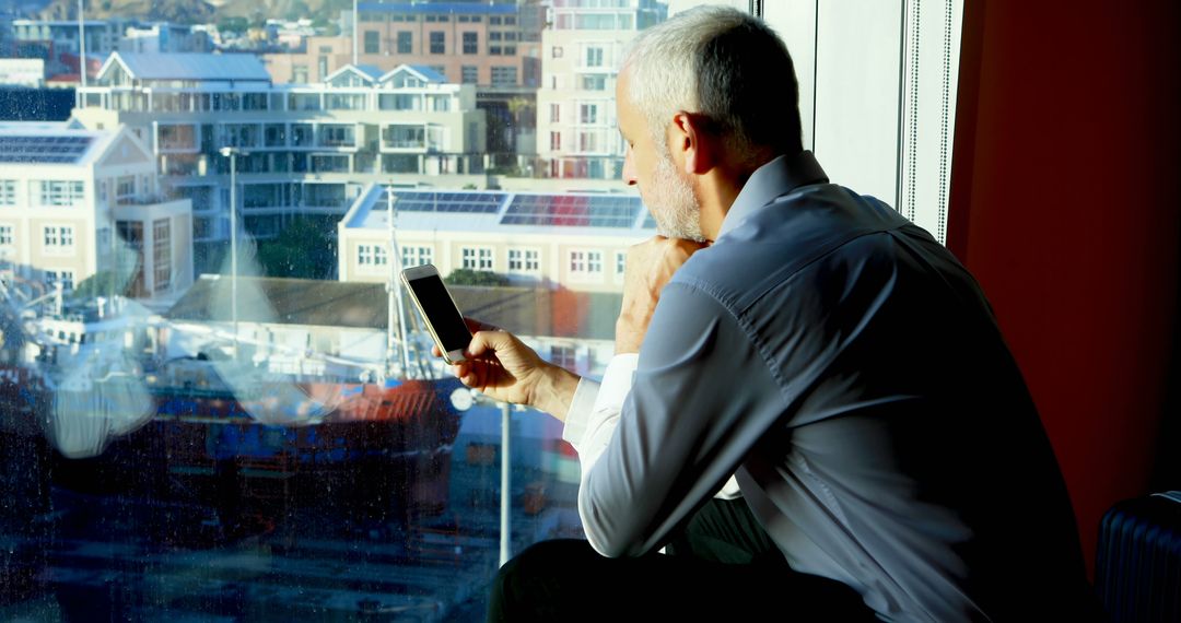 Businessman Checking Schedule on Smartphone by Window Desk - Free Images, Stock Photos and Pictures on Pikwizard.com