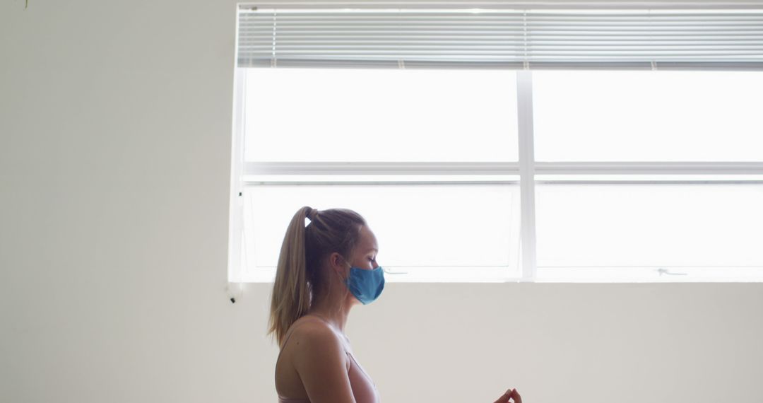 Woman Meditating Indoors Wearing Face Mask By Window - Free Images, Stock Photos and Pictures on Pikwizard.com