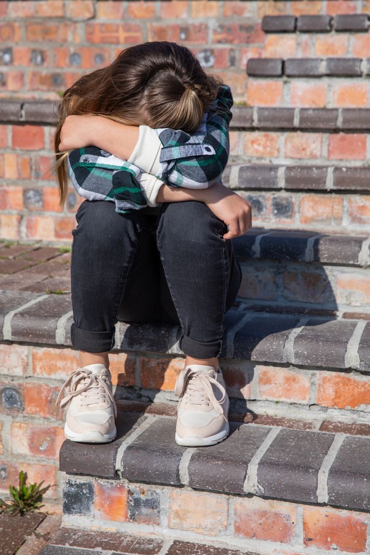 Teen Girl Sitting on Brick Steps Hugging Knees in Plaid Shirt