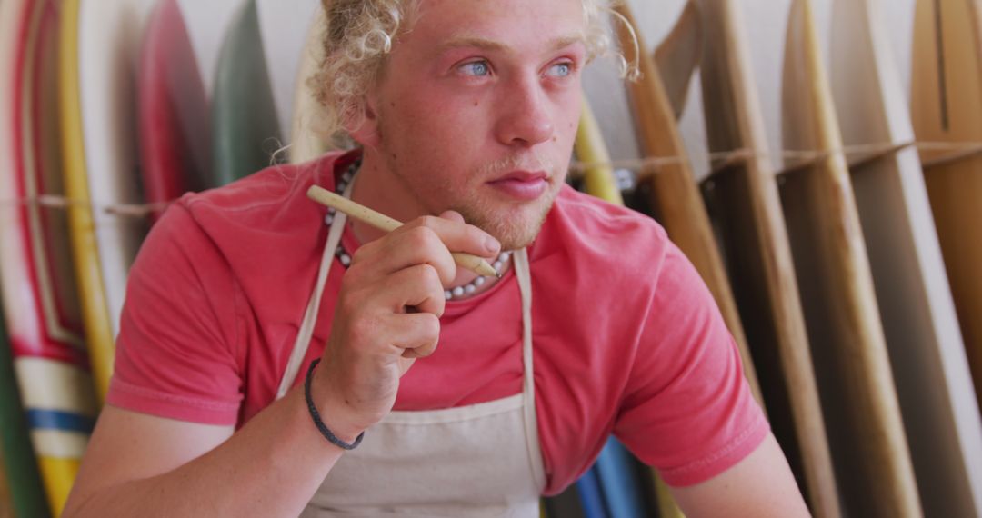 Young male surfboard craftsman contemplating - Free Images, Stock Photos and Pictures on Pikwizard.com