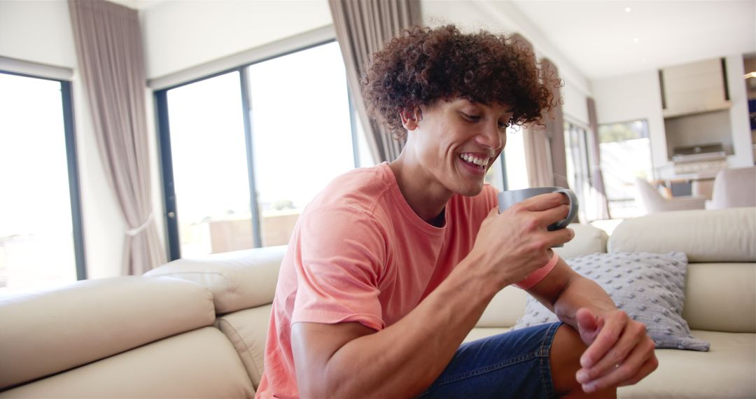 Young Man Smiling at Smartphone While Relaxing on Sofa at Home