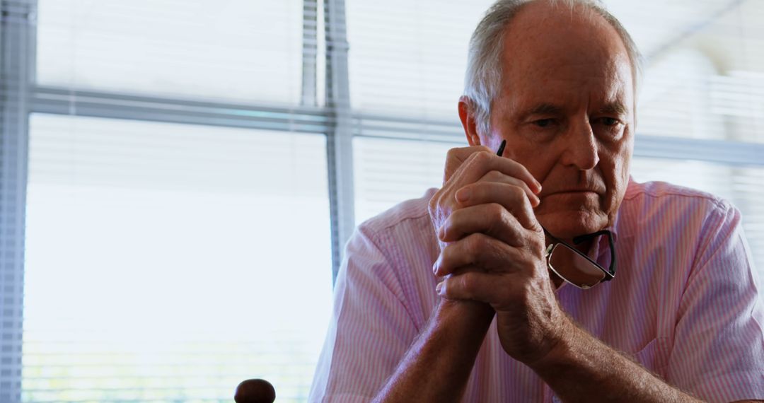 Pensive Elderly Man Contemplating with Glasses in Hand