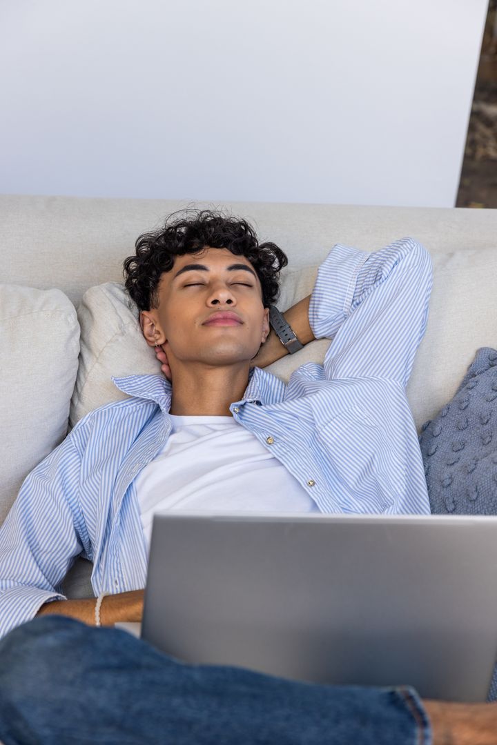Elegant Young Man Relaxing on Sofa with Laptop in Minimalist Living Room
