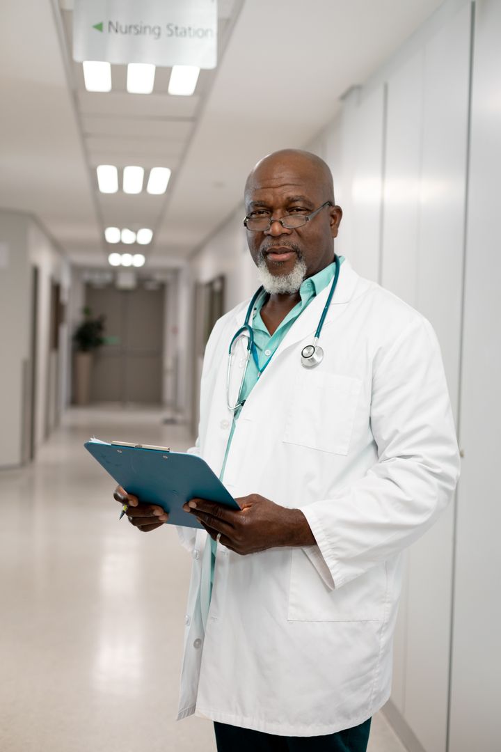 Senior African American Doctor Holding Clipboard in Hospital Corridor - Free Images, Stock Photos and Pictures on Pikwizard.com