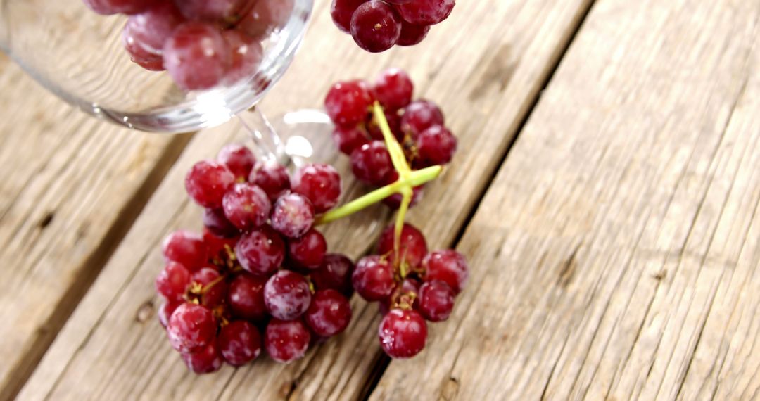 Red grapes spill from a tipped wine glass onto a wooden surface, with copy space - Free Images, Stock Photos and Pictures on Pikwizard.com