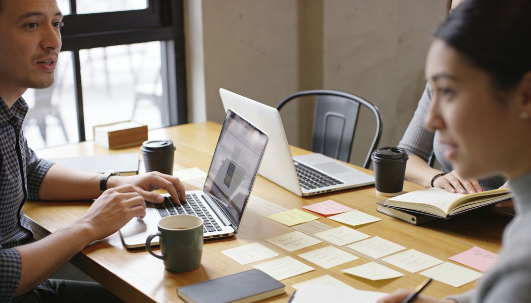 Creative team collaborating with laptops and sticky notes in modern coworking workspace