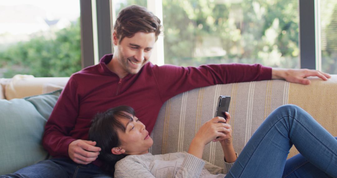 Image of back view of happy diverse couple sitting on sofa with smartphone - Free Images, Stock Photos and Pictures on Pikwizard.com