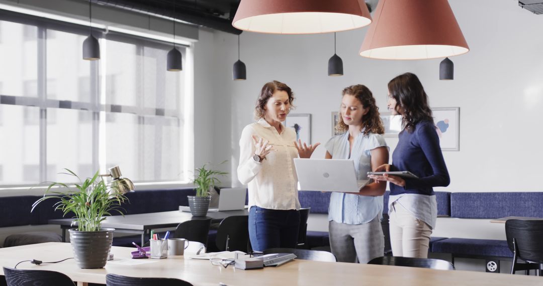 Diverse Women Collaborating in Modern Office Using Laptop