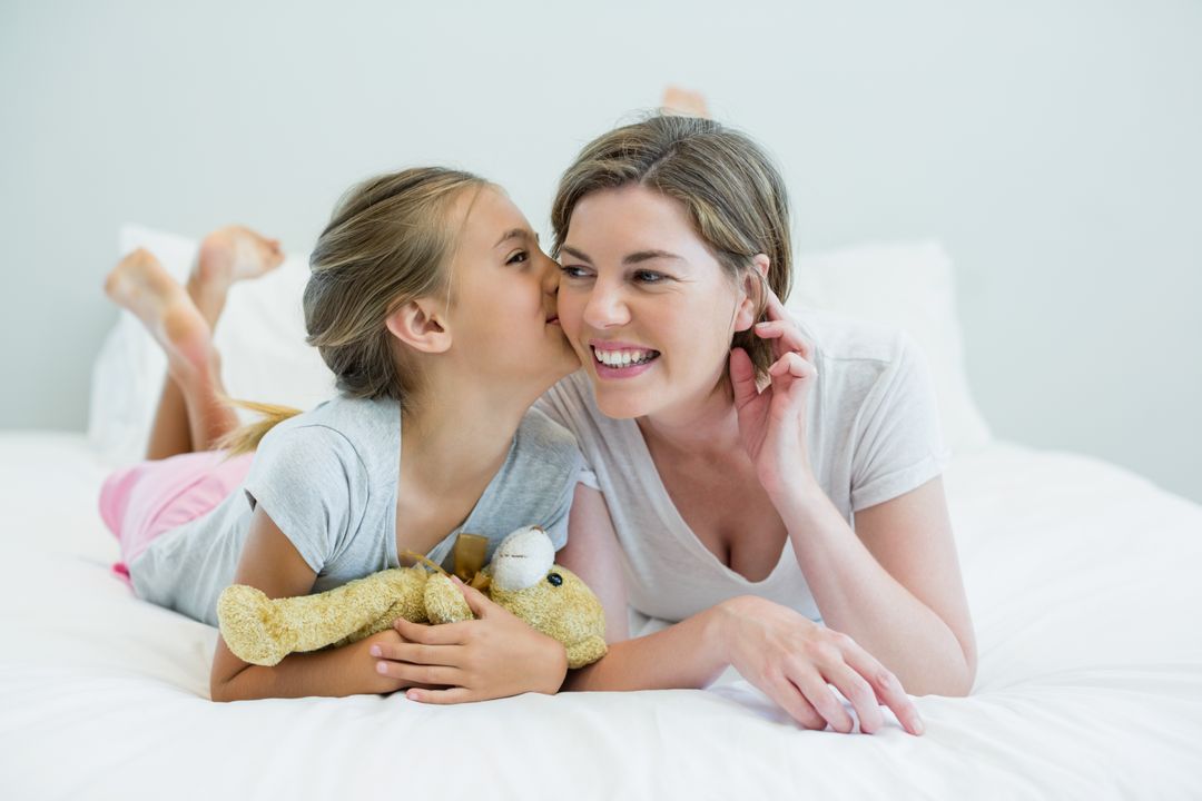 Adorable girl kissing her mother lying on a bed - Free Images, Stock Photos and Pictures on Pikwizard.com