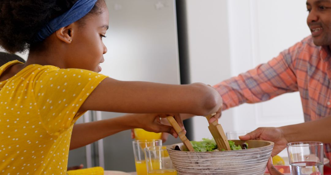 Young girl serving fresh salad while family enjoys meal together at home - Free Images, Stock Photos and Pictures on Pikwizard.com