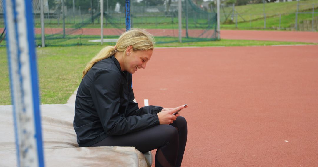 Female Athlete Relaxing with Smartphone at Track and Field Venue