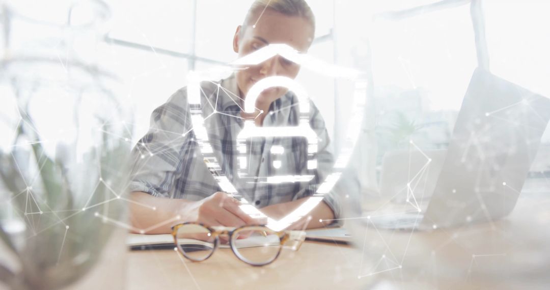 Woman writing at desk with digital shield overlay representing cybersecurity and privacy
