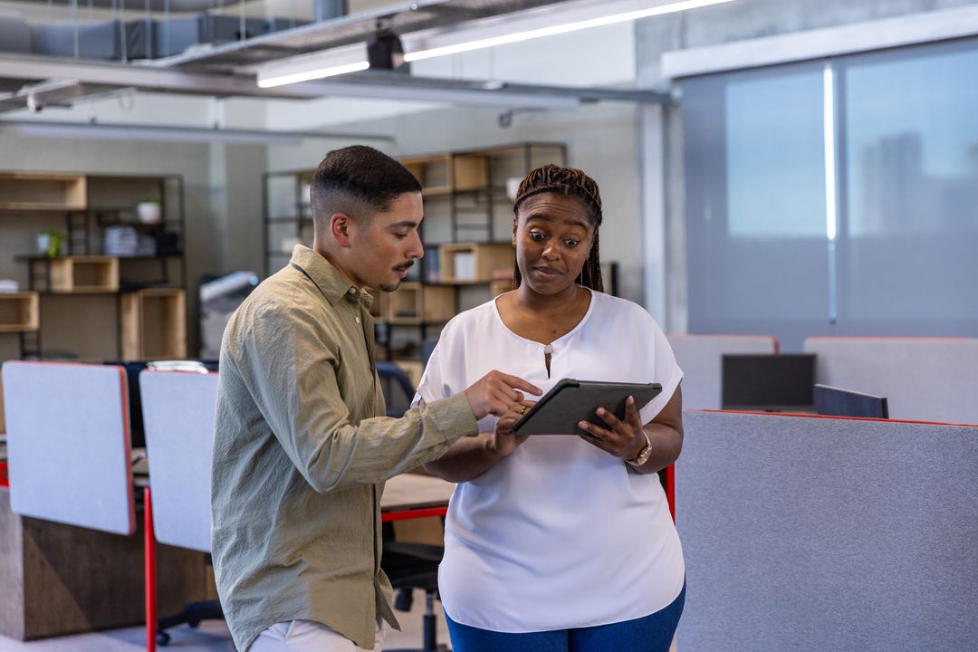 Diverse Coworkers Collaborating on Tablet in Modern Open Office