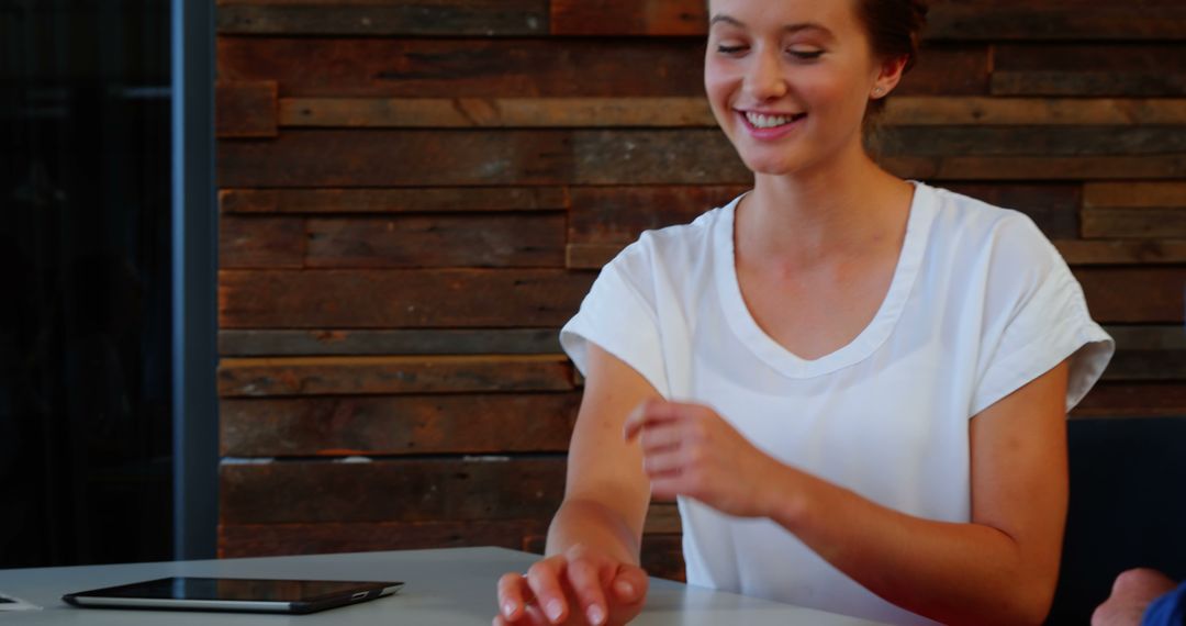 Smiling Woman in White Shirt Sitting at Desk with Wooden Wall Background - Free Images, Stock Photos and Pictures on Pikwizard.com