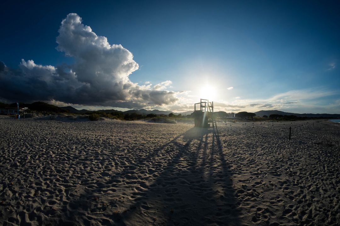 Sunset casting long lifeguard tower shadows across empty sandy beach with dramatic clouds