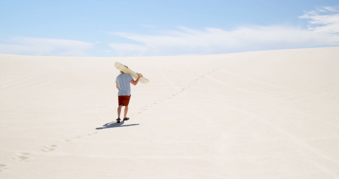 Man walking on sand dunes with snowboard under blue sky - Free Images, Stock Photos and Pictures on Pikwizard.com