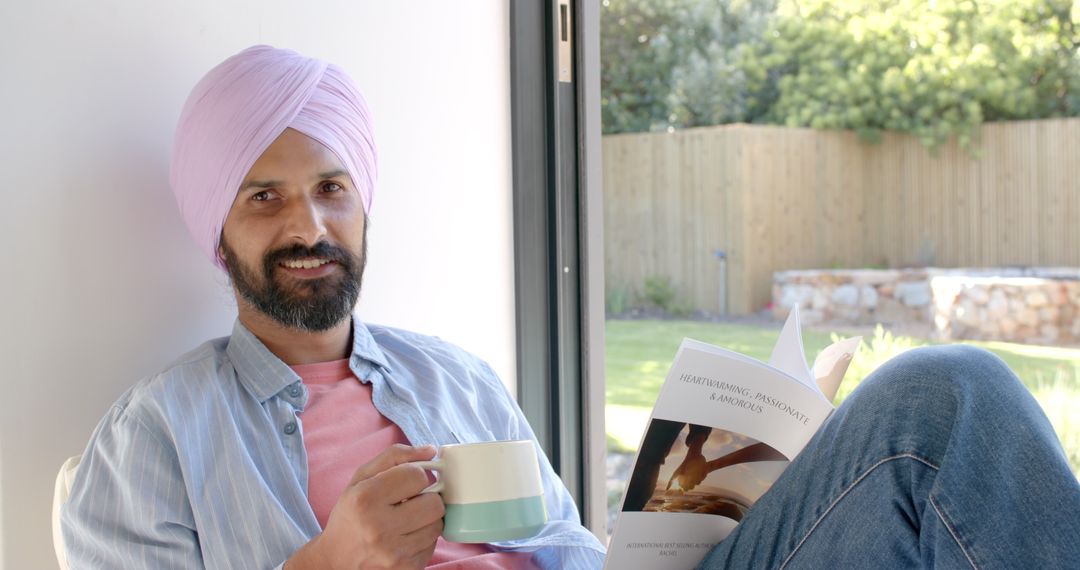 Man in Turban Drinking Coffee and Reading Book by Window
