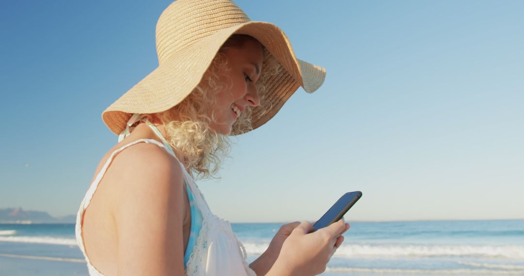 Woman in Sun Hat Using Smartphone at Beach - Free Images, Stock Photos and Pictures on Pikwizard.com